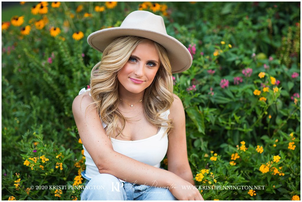 portrait of a Senior girl wearing a hat sitting in flowers