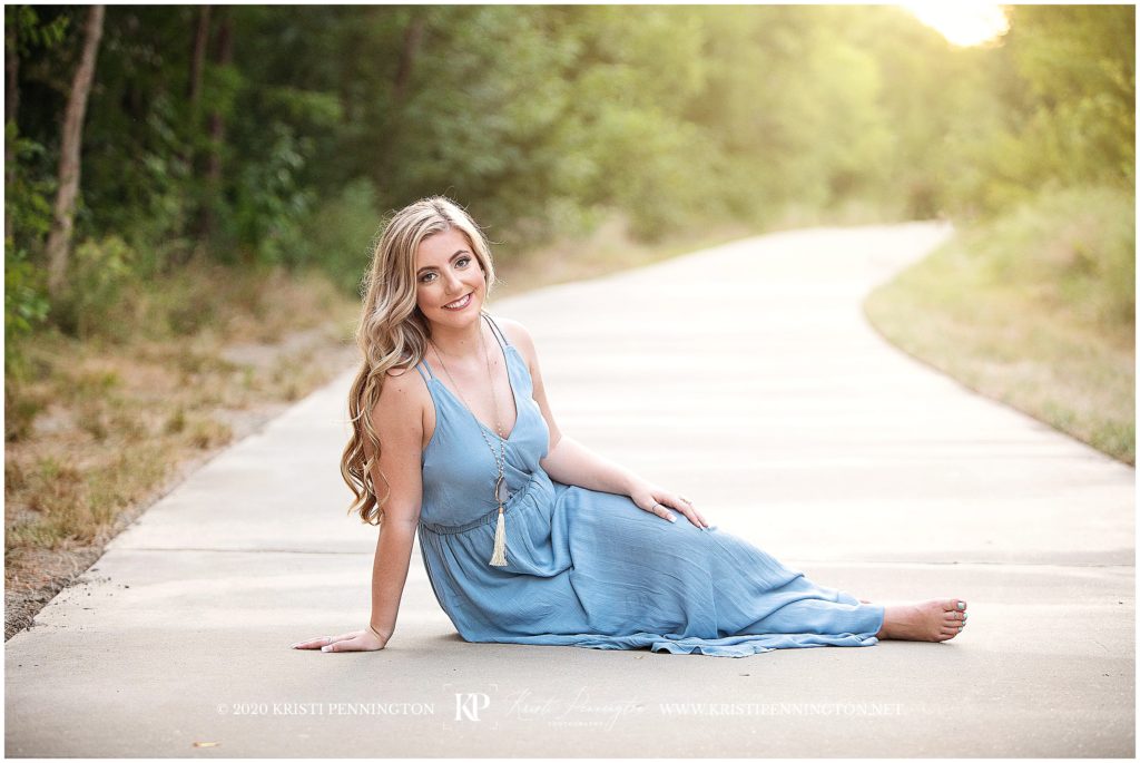 Senior girl sitting in light blue maxi dress on garden trail
