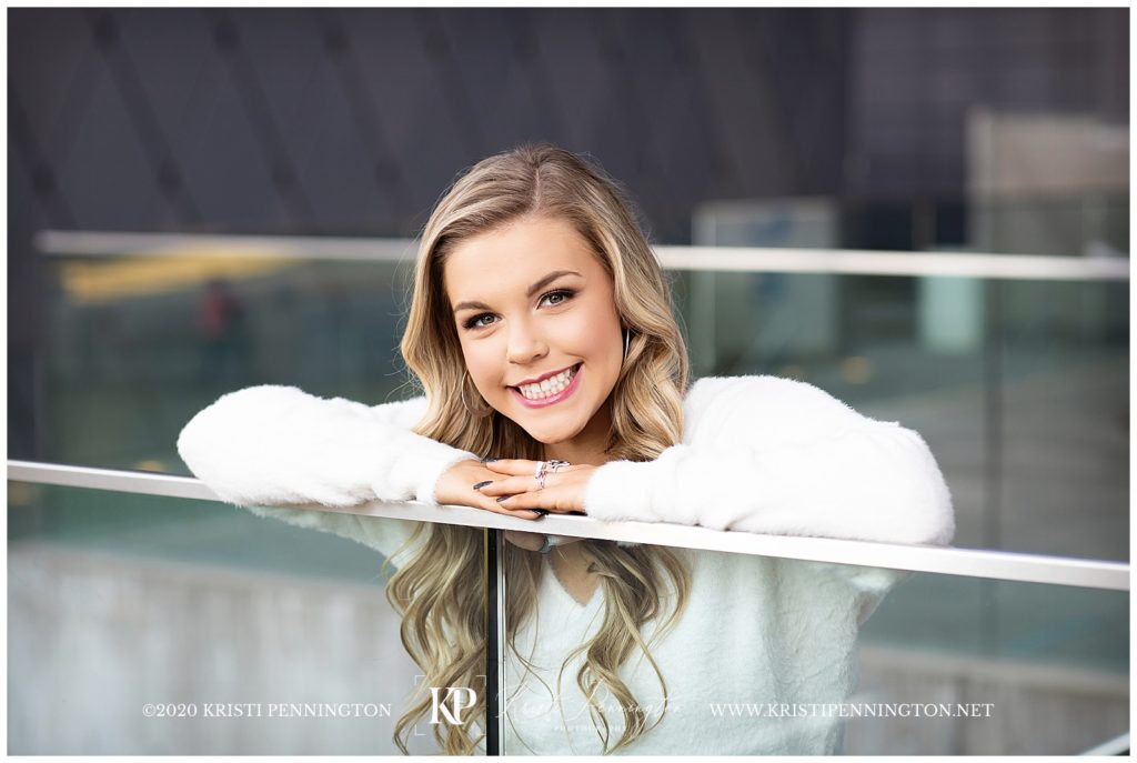 Uptown Girl Senior portraits in downtown Dallas leaning on glass railing at Winspear 